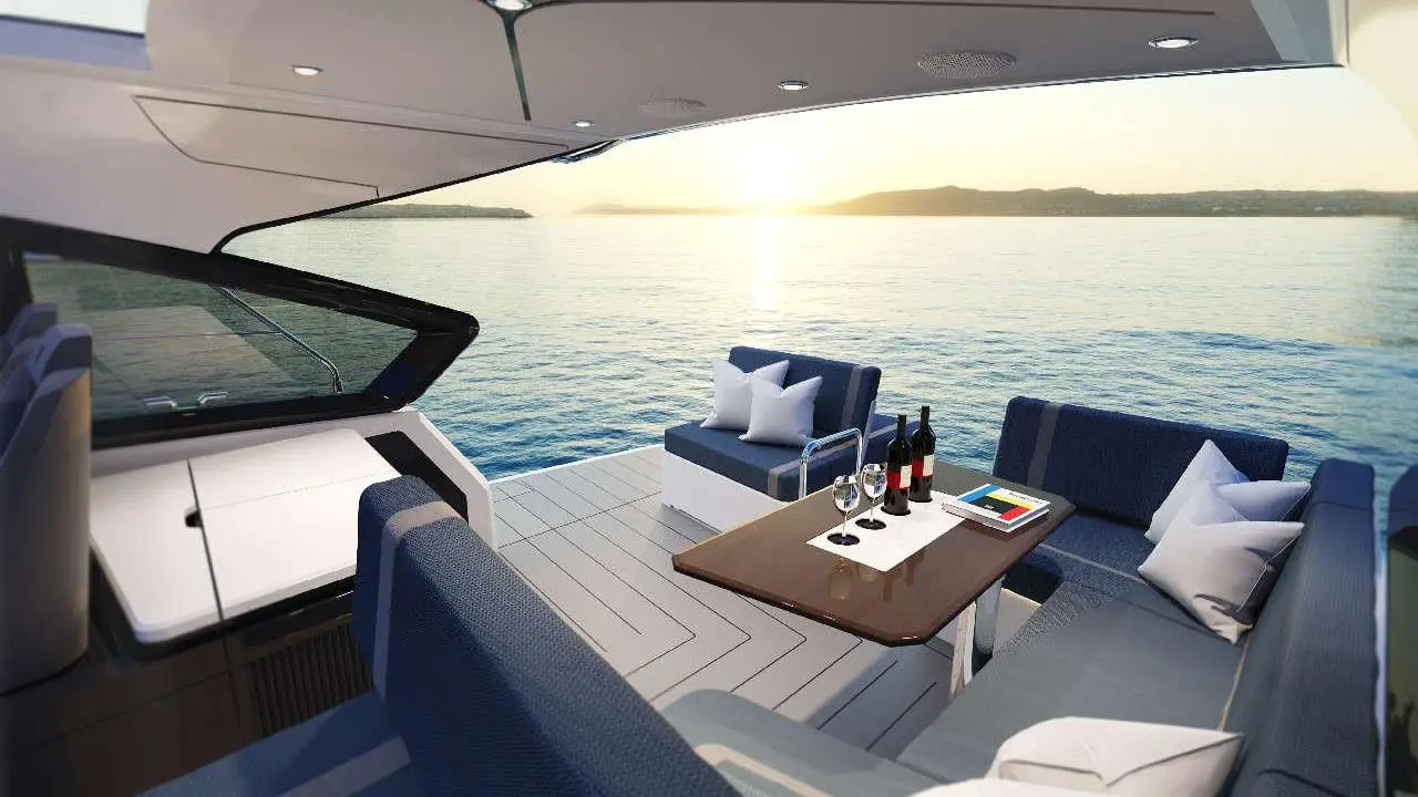 Luxurious yacht interior with plush seating, a table with wine bottles, and sunset views over calm water.